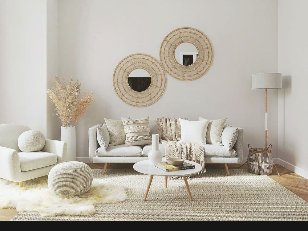 A pale living room with a sofa, a low round table and two woven mirrors.